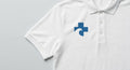 White piqué polo with the Beach Recovery Cross embroidered on the right chest beside the three-button placket.