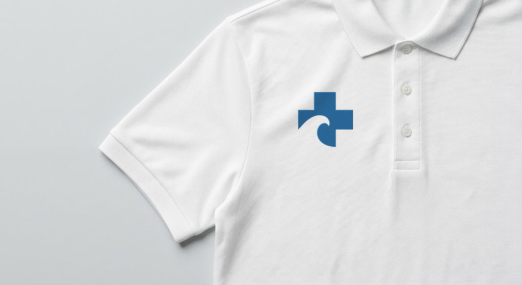 Close crop of the white piqué polo showing the embroidered Beach Recovery Cross on the right chest beside the three-button placket.