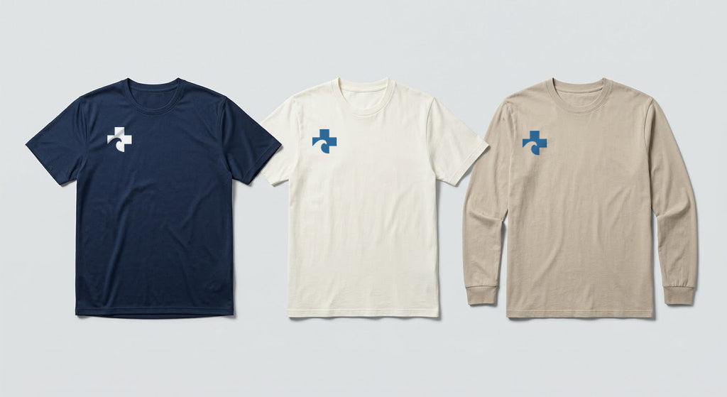 Three tees in a row in the three permitted colorways: navy athletic tee, off-white short sleeve, sand long sleeve, each carrying the Cross at the right chest.
