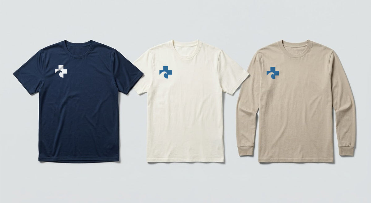 The sand long sleeve tee shown alongside the navy athletic tee and off-white short sleeve, each carrying the Cross at the right chest.