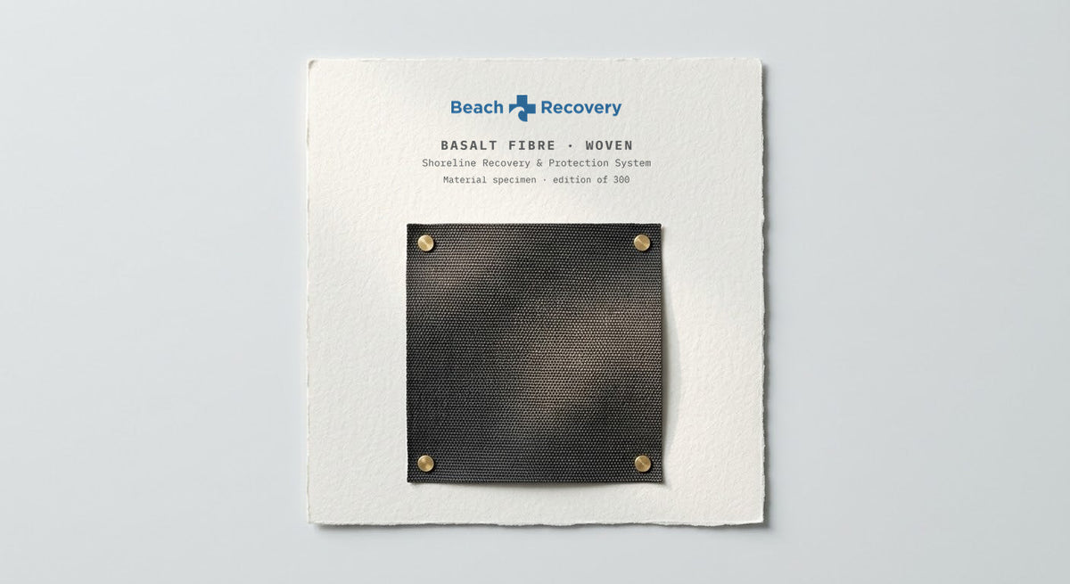 The basalt material specimen pinned at four corners to a printed spec card carrying the Beach Recovery signature.